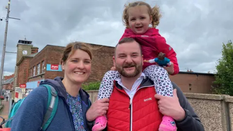 A picture of a smiling couple with a little girl on his shoulders
