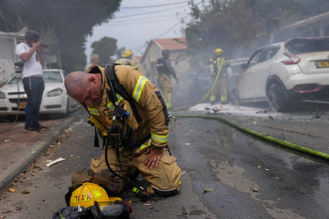 An Israeli firefighter kneels to recompose after he and his colleagues extinguished cars set on fire by a rocket fired from the Gaza Strip in Ashkelon, Israel, Monday, Oct. 9, 2023.