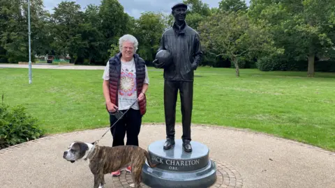 BBC A woman with a boxer cross stands next to a statue to Jack Charlton