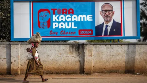 AFP A woman carrying her baby on her back walks past an electoral billboard asking for the vote for the incumbent President of Rwanda and the ruling Rwandan Patriotic Front (RPF) presidential candidate Paul Kagame in Kigali, on July 11, 2024