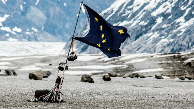 The state flag of Alaska fluttering in front of a mountainous open space..