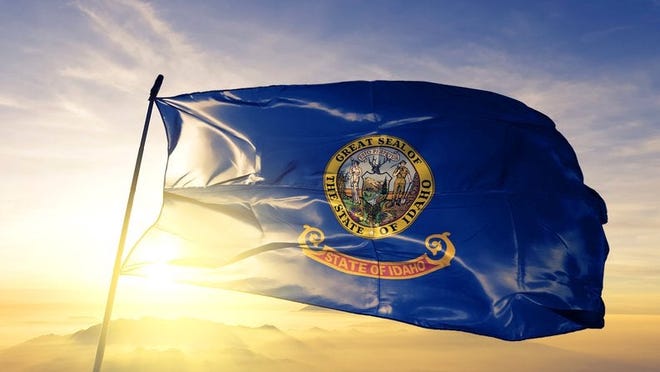 The Idaho state flag flying in front of a sunny sky.