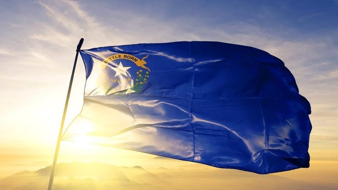 The state flag of Nevada flying in front of a sunny sky.