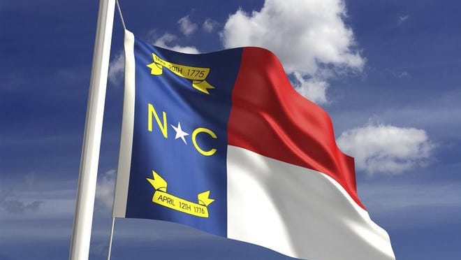 The North Carolina state flag in front of a blue sky with white clouds.