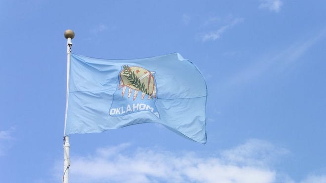 The Oklahoma state flag in front of a blue sky and white clouds.