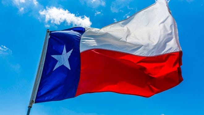 The state flag of Texas flying in front of a bright blue sky.