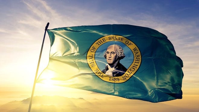 The state flag of Washington flying in front of a sunny sky.