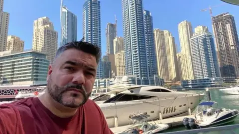 BBC Doede Osman Khan takes a selfie in front of skyscrapers and yachts