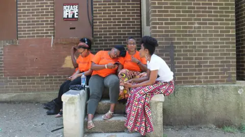 BBC Erricka Bridgeford, right centre, sits with her friend Ellen Gee, right, and her children outside of an abandoned rowhouse