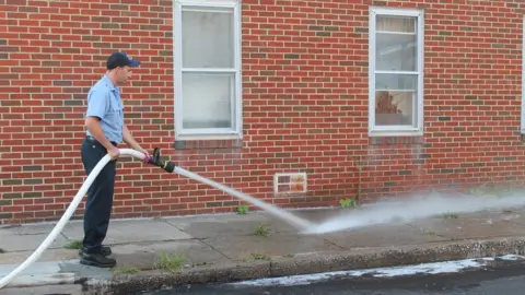BBC A Baltimore firefighter washes blood off of the sidewalk