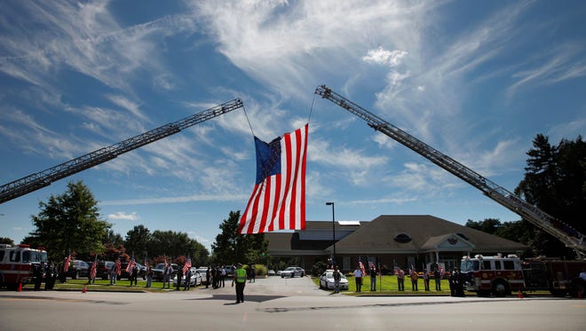 A large American flag flies over the entrance to the calling hours for slain Officer Daryl Pierson as the Patriot Guard lines Vintage Rd in front of the Bartolomeo & Perotto Funeral Home in Greece.