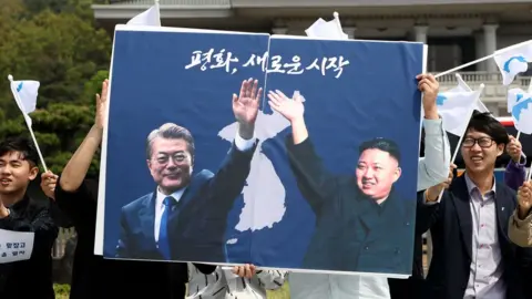 Getty Images Students hold posters with pictures of South Korea"s President Moon Jae-in and North Korea"s leader Kim Jong Un during a pro-unification rally