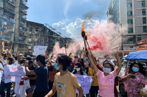Getty Images Women holding banners, emergency flare sticks and fire sticks as they march during a demonstration against the military coup in Yangon on July 14, 2021.