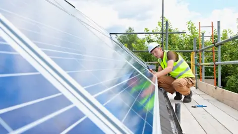 Getty Images A man fitting solar power panels to a roof