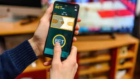Getty Images Hands holding a phone with a betting app on it.
