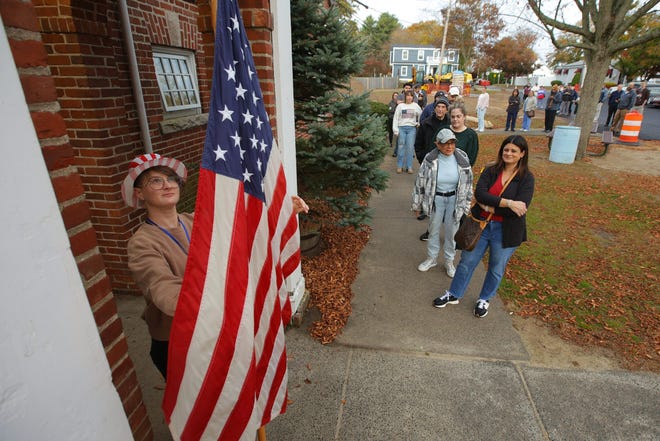 Rebeka Plaskon installs an American flag in front of the Buttonwood Warming House polling station in New Bedford, Mass., as voters wait for the polling station to open on Nov. 5, 2024.