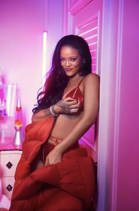 Savage X Fenty  Rihanna smiles in her latest collection for Savage X Fenty in red satin bra set and a red long puffer jacket