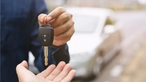 Getty Images A man handing car keys to a new car owner