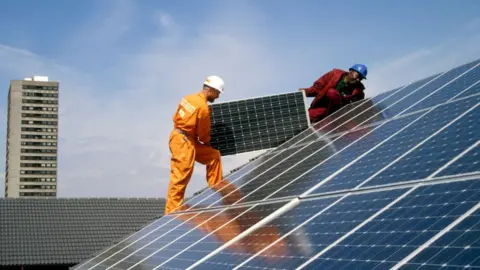 Getty Images Engineers fitting solar panels to a roof at Silvertown Solar Village, Docklands, London UK