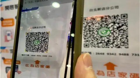 Getty Images A local resident scans a QR code of a government-made app to register her personal identity before entering a shopping mall in New Taipei City