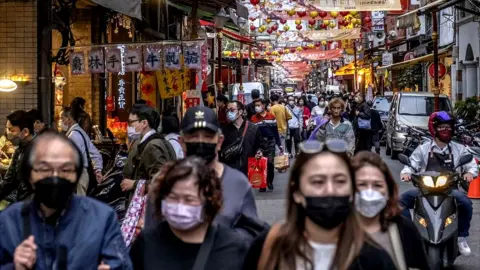 Getty Images People wear protective face masks while shopping for Lunar New Year goods on January 27, 2022 in Taipei, Taiwan.