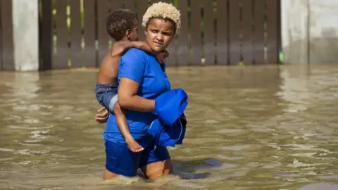 Getty Images Woman carrying child wades through flooded street