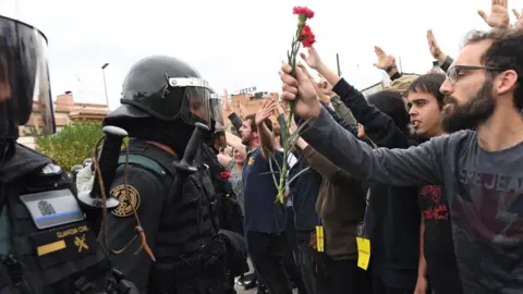 Getty Images Crowds raise their arms up and a man holds red and pink flowers as police move in on members of the public gathered outside to prevent them from voting in the referendum at a polling station( October 1, 2017)
