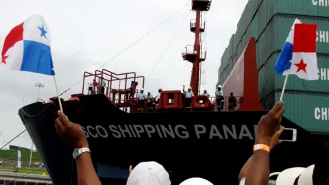 Getty Images A person hold Panama flags in front of a ship docked in the Panama canal