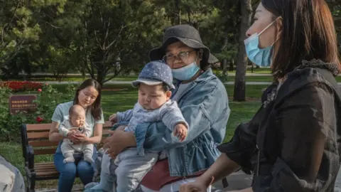 Getty Images Women hold their babies as they talk at a local park on 12 May 2021 in Beijing, China.