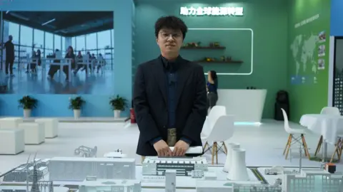 Wang Xiqing/BBC Man stands in front of model of buildings at energy expo