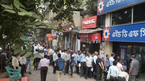 Getty Images People stand in a queue in front of a private sector bank during a nationwide strike called by major trade unions to protest against demonetisation in Kolkata on November 28, 2016