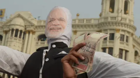 Getty Images A man holds up 1000 rupee notes against a prop of Modi