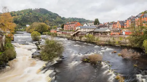 Getty Images Fast flowing wide river, with white foam, behind it Llangollen town, including its heritage train station