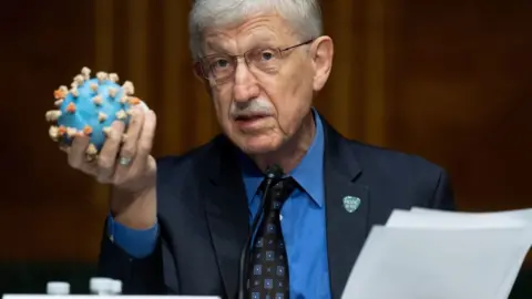 Getty Images Director of the National Institutes of Health, Dr. Francis Collins, holds a model of the coronavirus as he testifies at a US Senate hearing to review Operation Warp Speed: the researching, manufacturing, and distributing of a safe and effective coronavirus vaccine, in Washington, DC, on July 2, 2020.