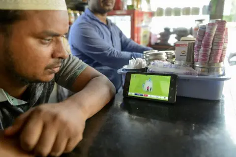 AFP An Indian fan watches a live broadcast of the Cricket World Cup match between India and Pakistan on a mobile phone at a paan shop (food preparation composed of betel leaf and areca nut) in Hyderabad on June 16, 2019.