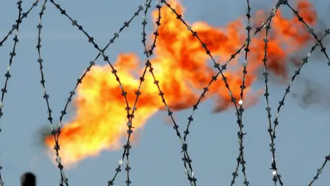 Getty Images A gas flame is seen behind a barbed wire in the former Yukos and current Rosneft oil company production plant in Prirazlomnoye, western Siberia