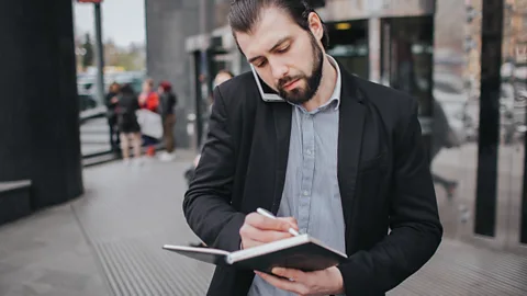 Alamy Man on phone writing notes while walking